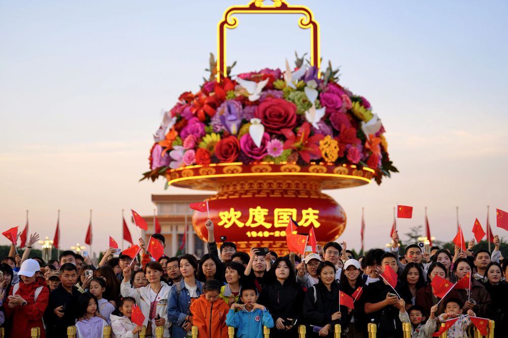 2025年10月1日,在北京天安门广场,人们观看升国旗仪式后挥舞国旗。